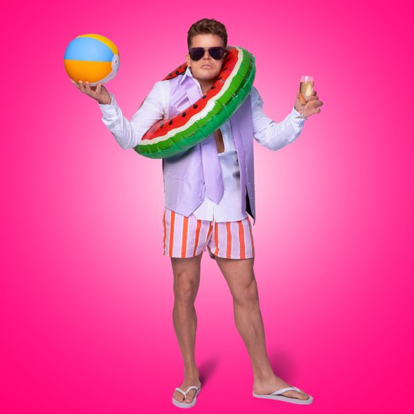 Giovanni Spano as Ash. He wears a shirt with lilac waistcoat and tie. He has sunglasses on, a watermelon pool float around him and holds a beach ball and a glass of Prosecco.